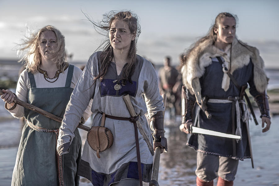 Three female vikings posing in front of a group of warriors stood in the surf on the shore Photograph by Lorado