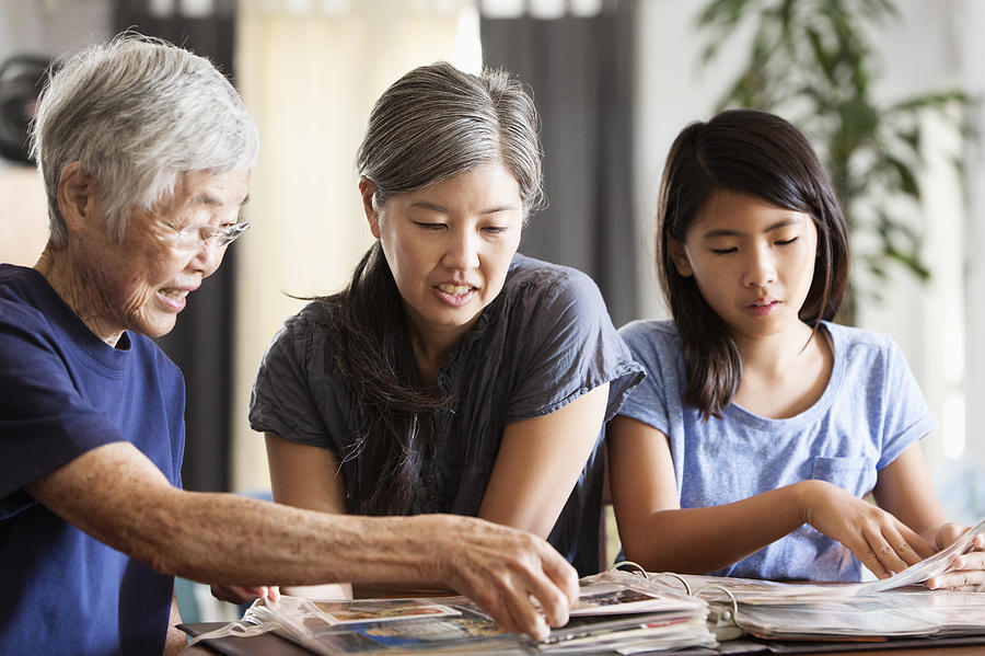 Three generations of Asian women looking at photo album Photograph by Hill Street Studios