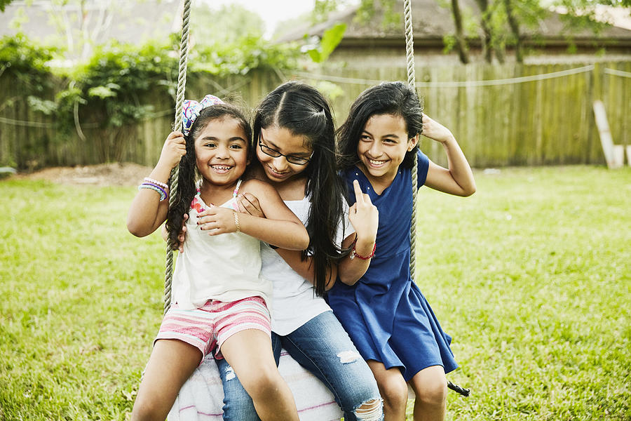 Three laughing female cousins swinging on swing in backyard Photograph by Thomas Barwick
