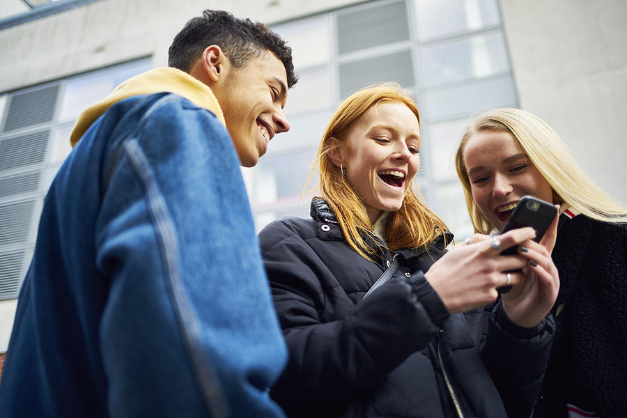 Three teens laughing and joking while looking at their phone Photograph by Justin Lambert
