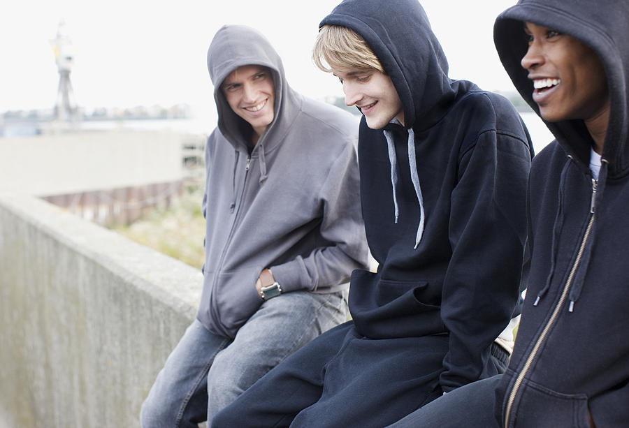 Three young men in hoodies sitting on wall Photograph by Paul Bradbury