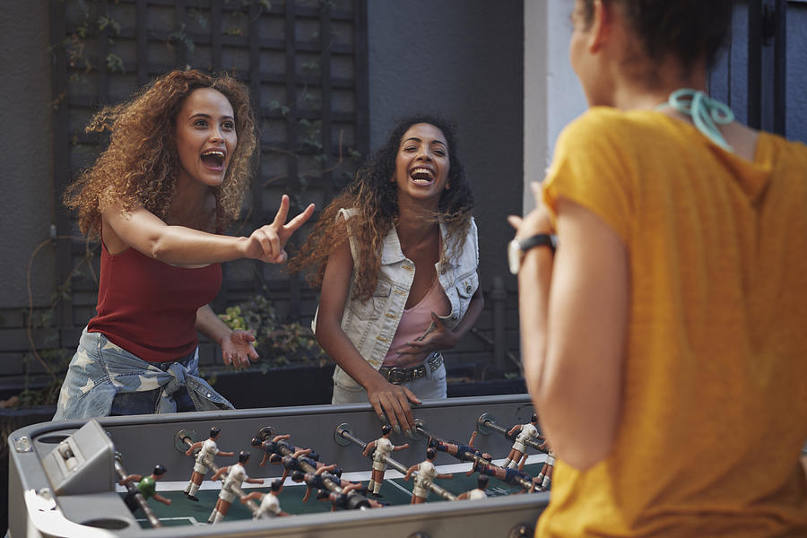 Three young women playing foosball at youth hostel Photograph by Klaus Vedfelt