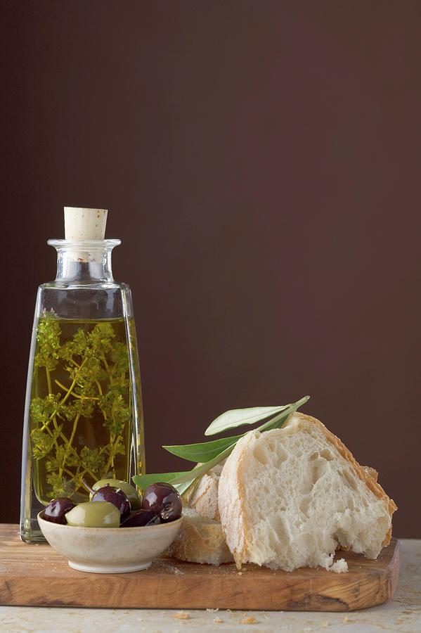 Thyme Oil In Bottle, Olives and White Bread On Chopping Board