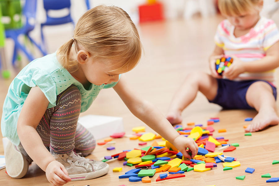 Toddler girls playing with puzzle pieces in a preschool classroom Photograph by SDI Productions