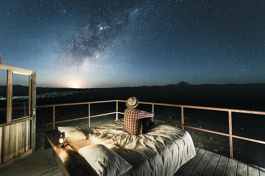 Tourist sitting in bed outdoors under a starry sky Photograph by © Marco Bottigelli