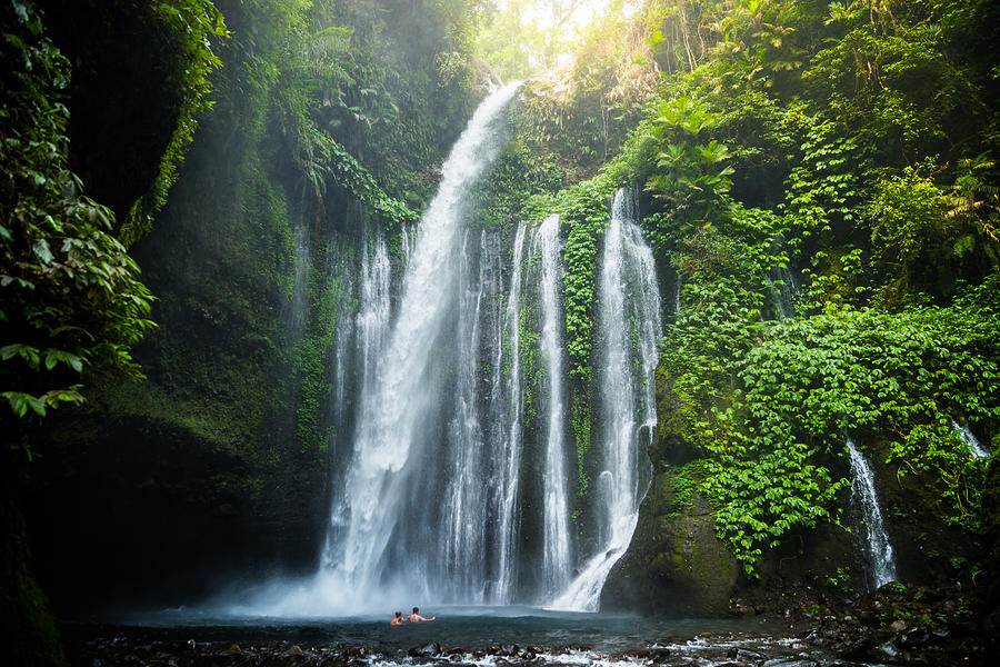 Traveler couple swimming in the beautiful wild waterfall in the deep rain forest of the national park of the Lombok island taken during travel vacations in Indonesia. Photograph by Artur Debat
