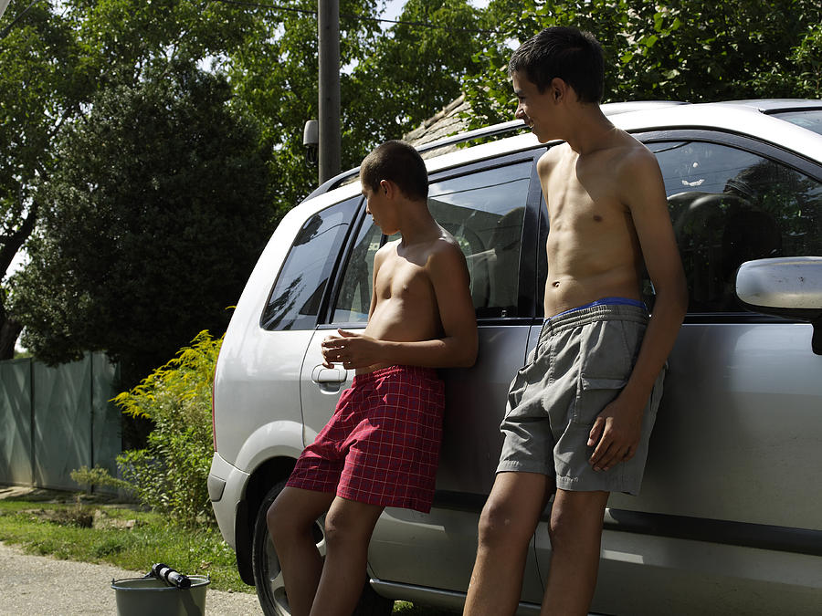Two boys (10-14) leaning against car Photograph by Adrian Samson
