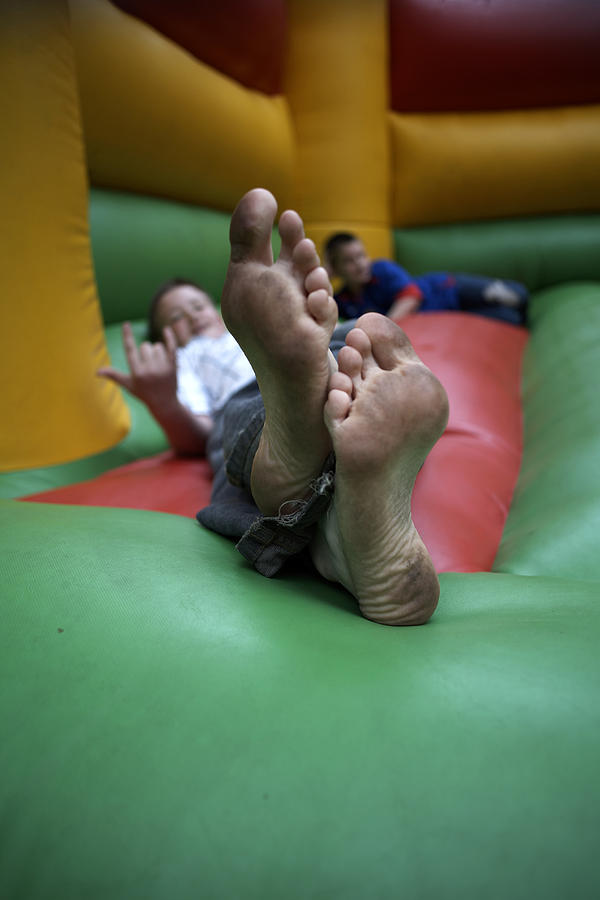 Two boys (11-14) with dirty feet lying in bouncy castle (focus on foreground) Photograph by Simon Bottomley