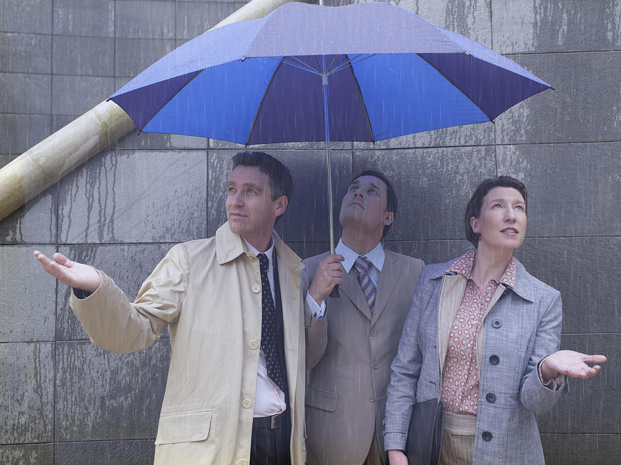 Two businessmen and woman sheltering under umbrella in rain Photograph by A J James