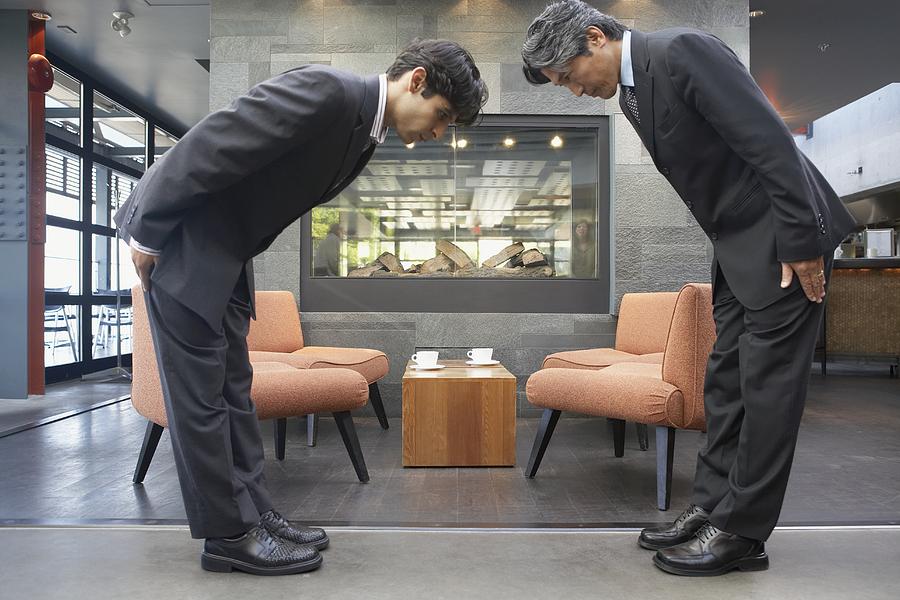 Two businessmen bowing to each other in cafe Photograph by Blend Images - Noel Hendrickson