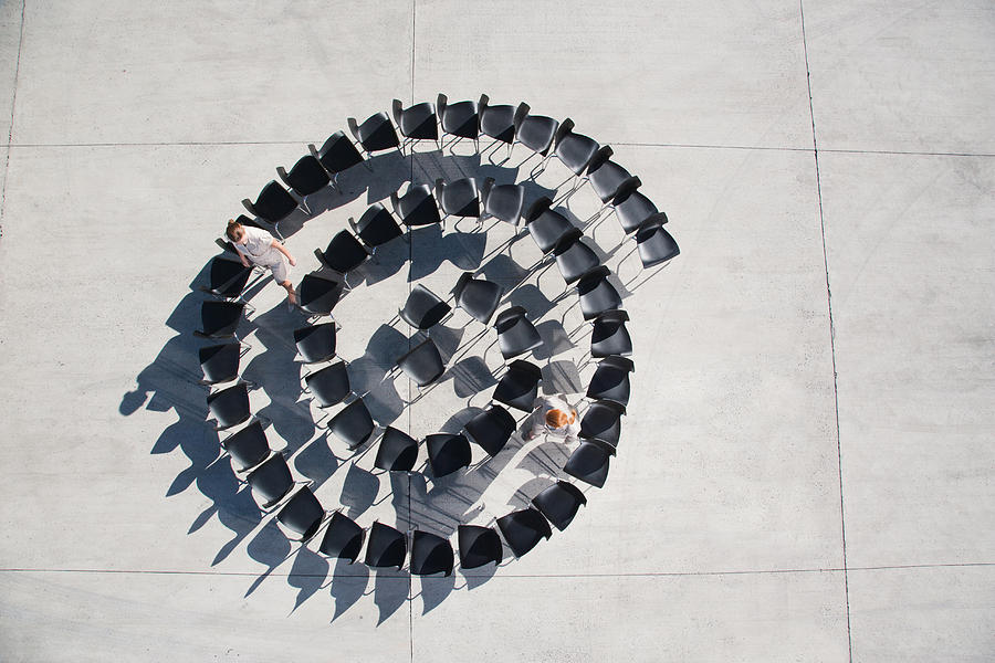 Two businesswomen standing with spiral of office chairs Photograph by Martin Barraud