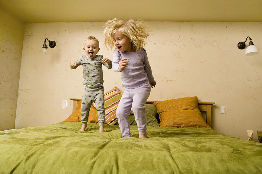 Two children (3-4), (4-5), jumping on bed Photograph by Photodisc