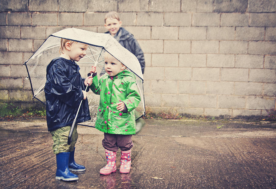 Two children sharing an umbrella in the rain Photograph by Sally Anscombe