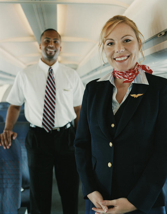 Two Flight Attendants Standing in the Cabin of a Plane Photograph by Digital Vision.