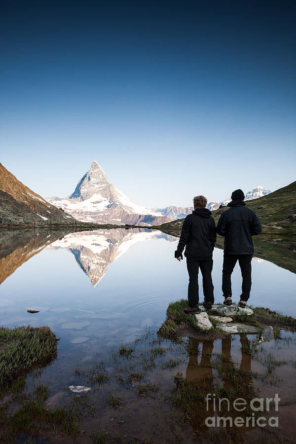 Two hikers looking at Matterhorn reflected in lake at sunrise Photograph by Matteo Colombo