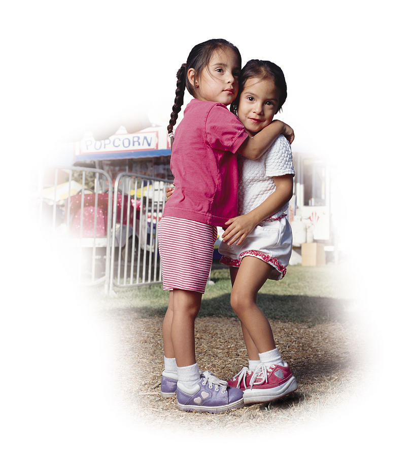 Two Little Hispanic Girls At A County Fair Are Wearing Pink And White Shorts And T-shirts As They Hug Each Other Photograph by Photodisc