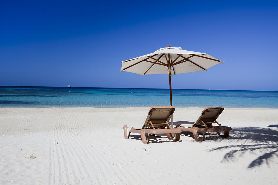 Two lounge chairs lying on a clear beach under a parasol Photograph by Dstephens