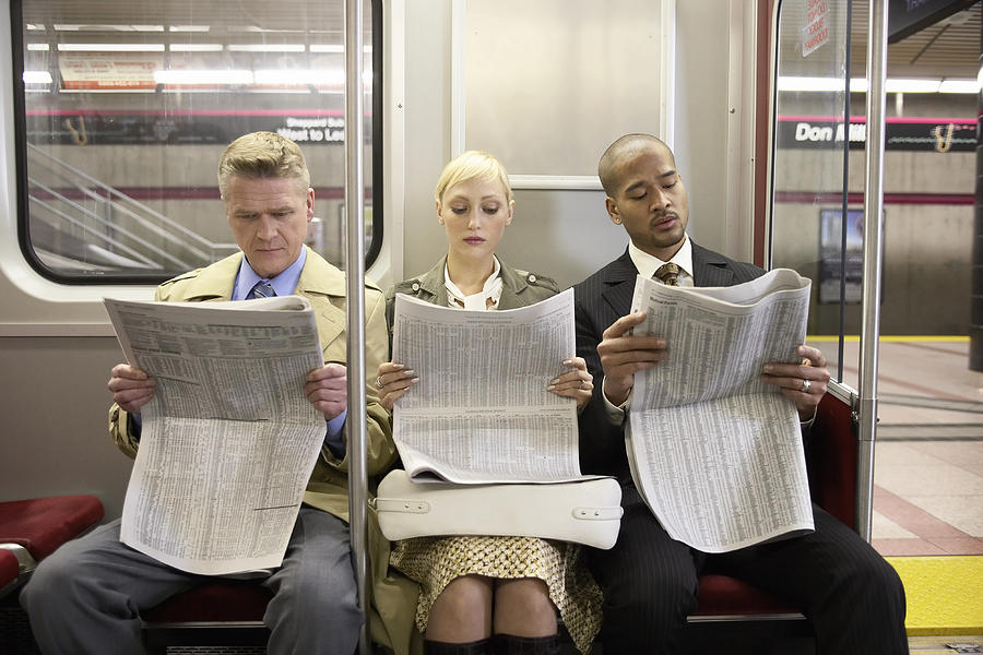 Two men and woman sitting in subway train side by side, reading newspaper Photograph by Darrin Klimek