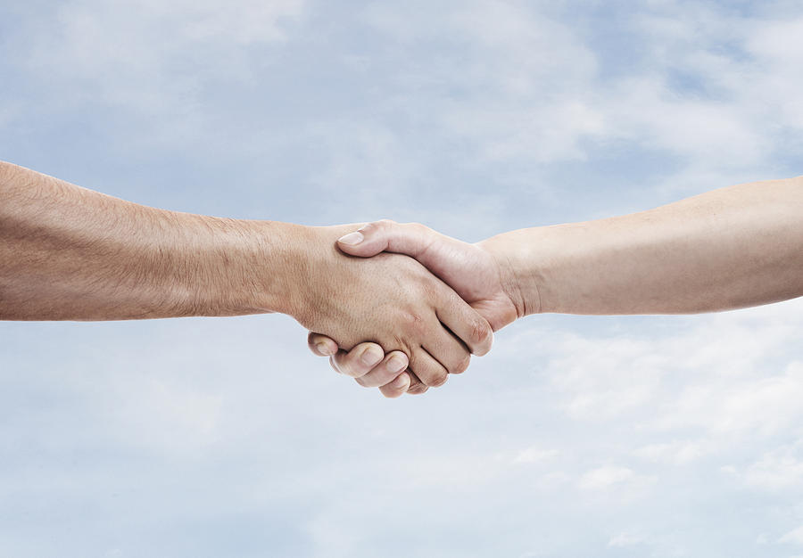 Two men shaking hands againt sky background Photograph by Paper Boat Creative