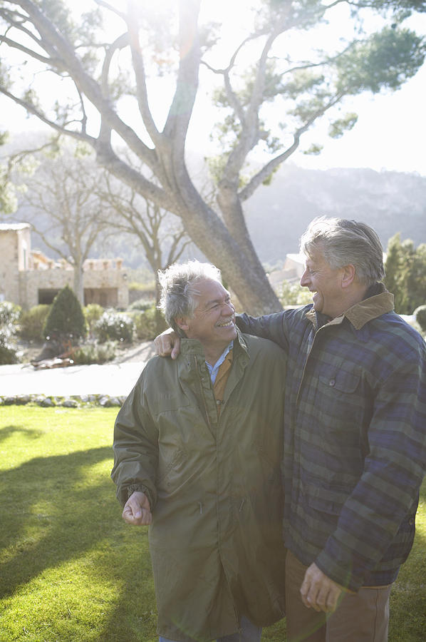 Two Senior Men Walk in the Garden With Their Arms Around Each Other, Talking and Smiling Photograph by Digital Vision.
