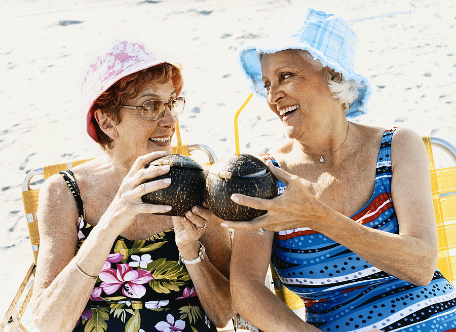 Two Senior Women Sit on the Beach Making a Toast With Coconut Cocktails Photograph by Digital Vision.