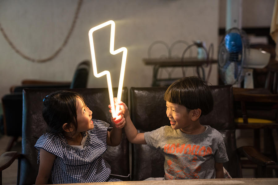 Two small children holding a lightning bolt shaped neon light Photograph by Trevor Williams