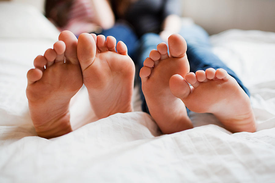 Two teenage girls lying on bed barefoot Photograph by Image Source