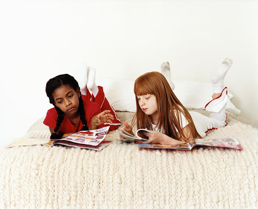 Two Teenage Girls Lying on Bed Reading Magazines Photograph by Lottie Davies