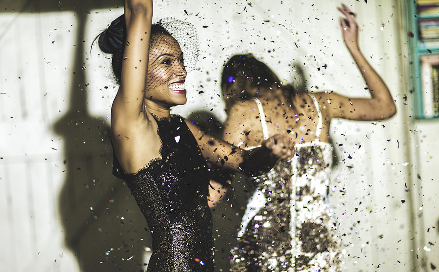 Two women wearing cocktail dresses at a party dancing in a shower of glitter confetti. Photograph by Mint Images