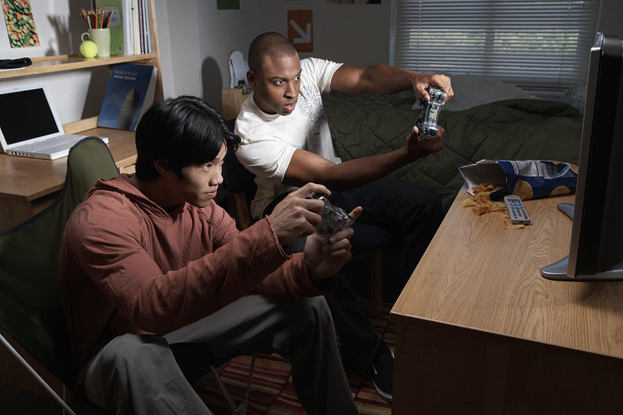 Two young men playing video game in dorm room, side view Photograph by James Woodson