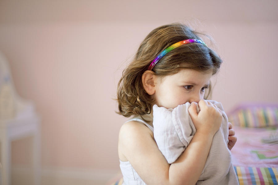 Unhappy three year old girl in bedroom holding comfort blanket to face Photograph by Sydney Bourne