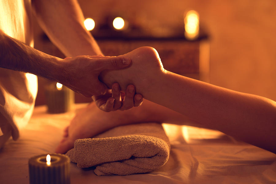 Unrecognizable massage therapist massaging womans foot at spa. Photograph by Skynesher
