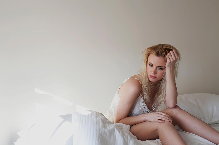 Upset young woman sitting on bed Photograph by Image Source