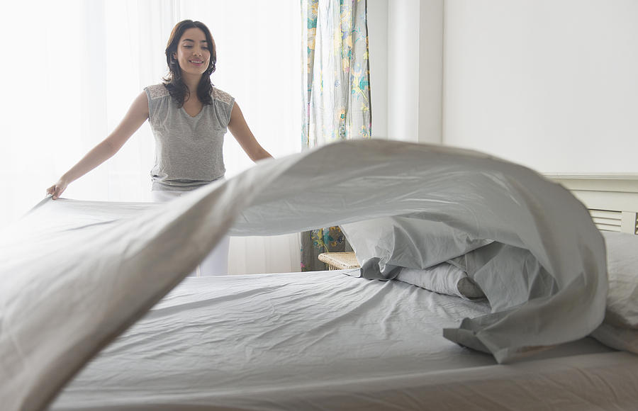 USA, New Jersey, Young woman spreading sheet on bed Photograph by Tetra Images