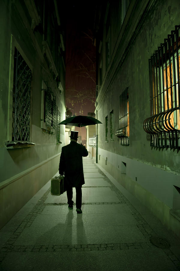 Victorian man with top hat carrying a suitcase and umbrella walking in the narrow street at night Photograph by Jaroslaw Blaminsky
