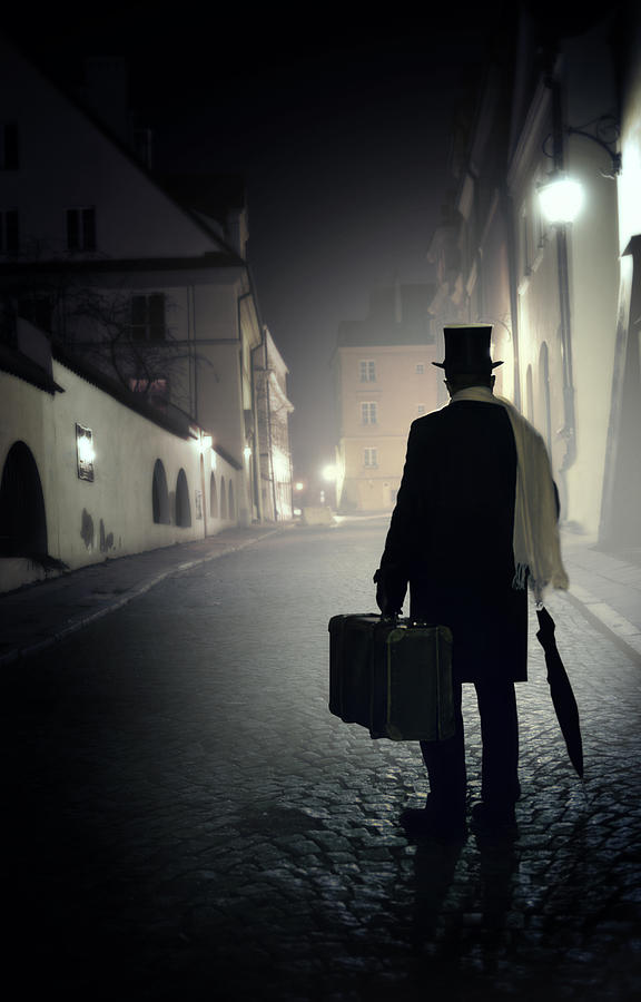 Victorian man with top hat carrying a suitcase walking in the old town at night Photograph by Jaroslaw Blaminsky