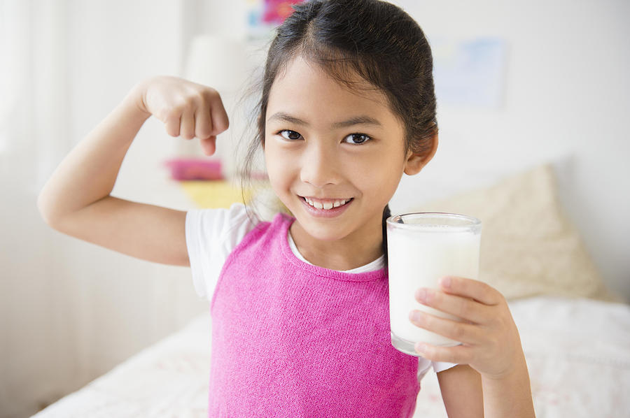 Vietnamese girl flexing muscles with glass of milk Photograph by JGI/Jamie Grill