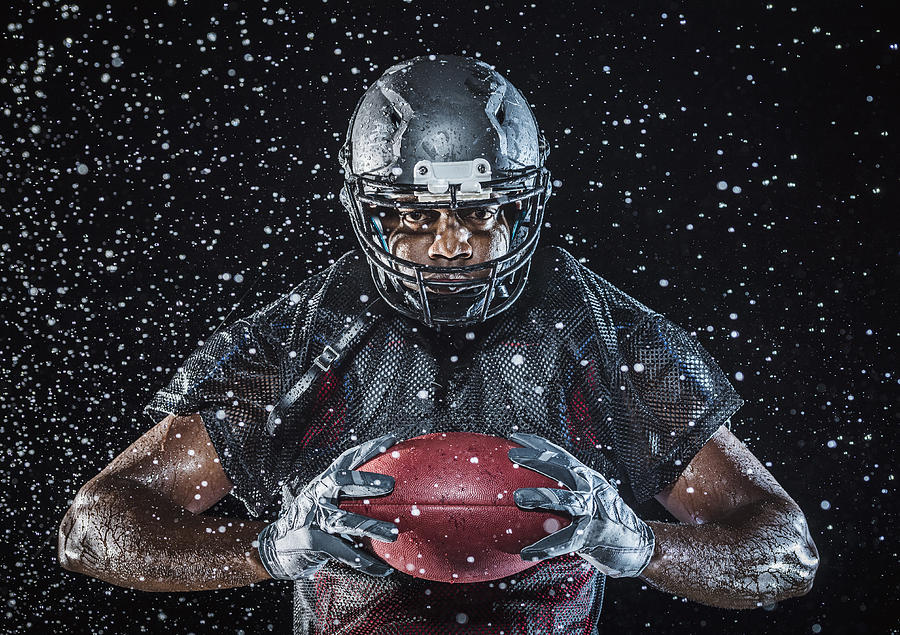 Water splashing on Black football player holding football Photograph by Erik Isakson