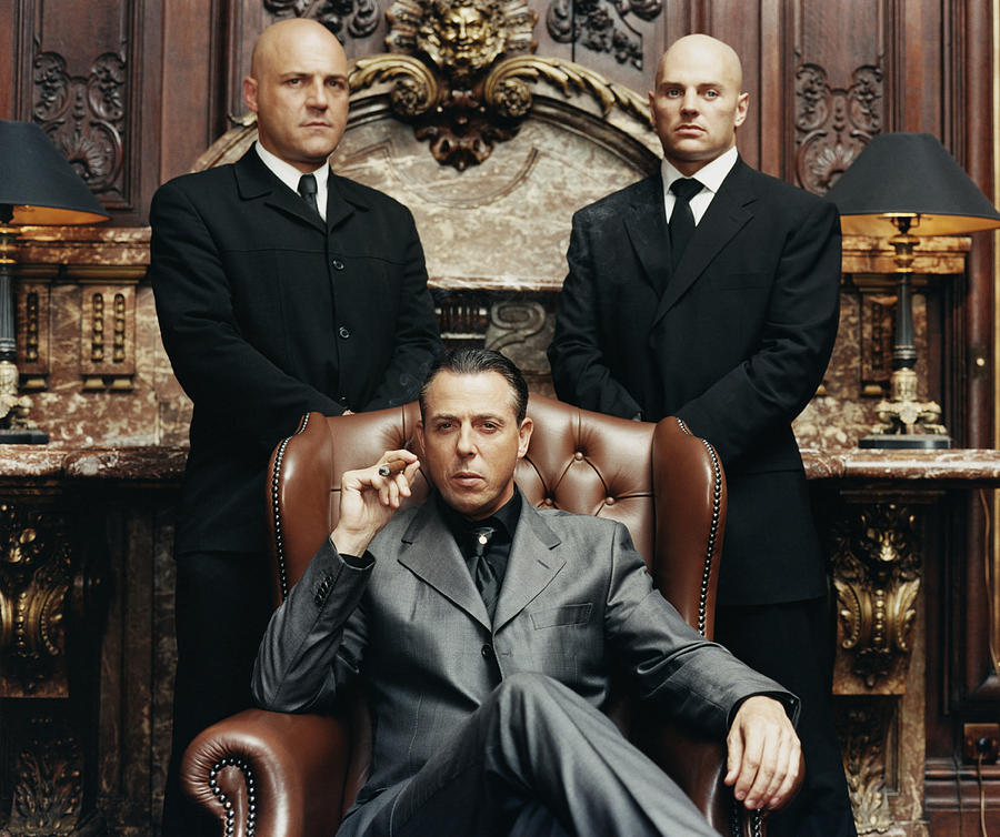 Wealthy Criminal Sitting in an Armchair Between two Bodyguards Photograph by Digital Vision.