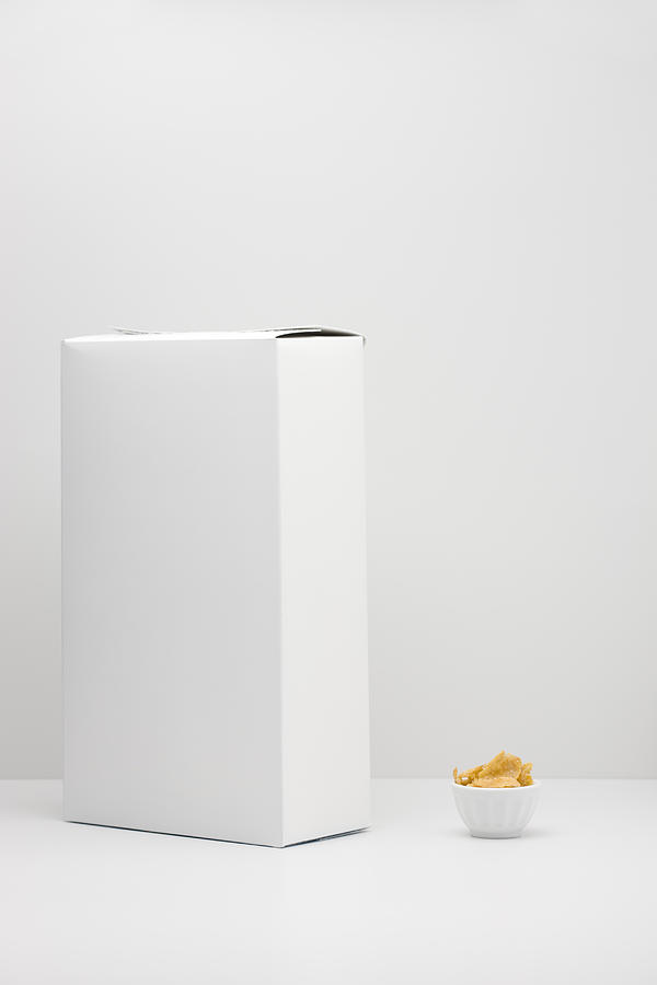 White cereal box and small bowl of cereal Photograph by PhotoAlto/Milena Boniek