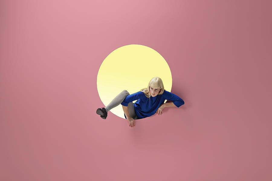 Woman crawling out of round opening in coloured wall Photograph by Klaus Vedfelt