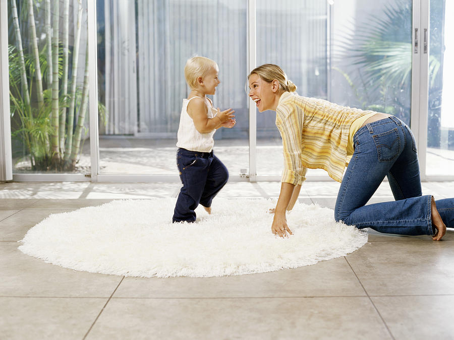 Woman crawling towards female toddler (21-24 months) on rug, side view Photograph by Kraig Scarbinsky