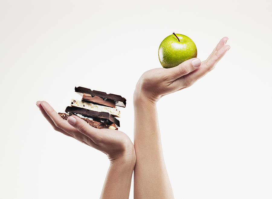 Woman cupping green apple above chocolate bars Photograph by Chris Ryan