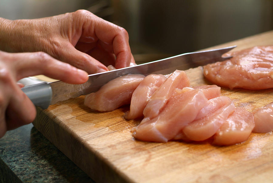 Woman Cutting Raw Chicken on a Wooden Cutting Board Photograph by Stephanie Phillips