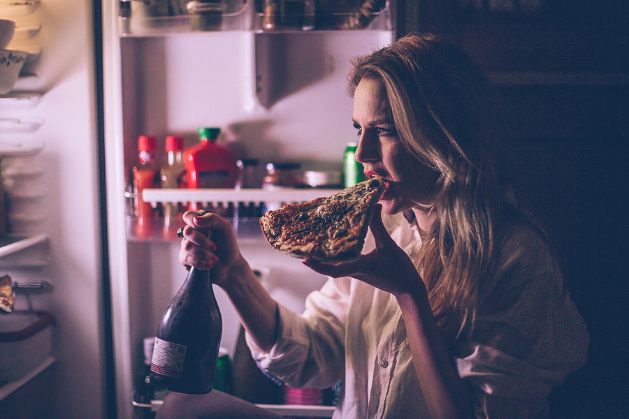 Woman eating pizza and drinking wine in front of the refrigerator during the night Photograph by Domoyega
