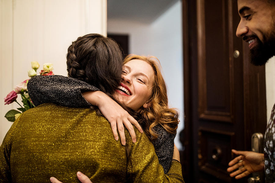 Woman embracing friend during visit for dinner party Photograph by Luis Alvarez