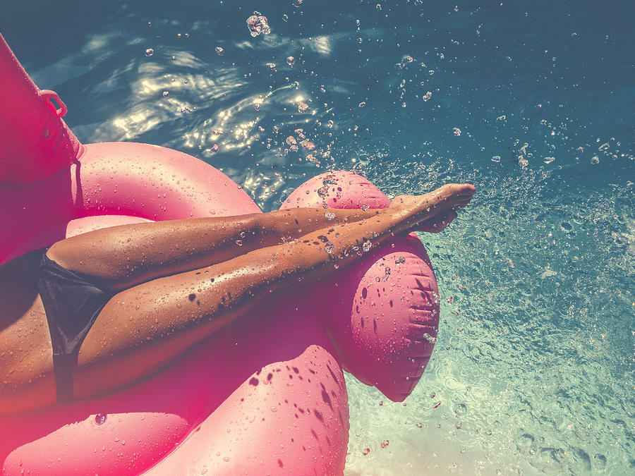 Woman floating on a pink inflatable in swimming pool. Photograph by Courtneyk