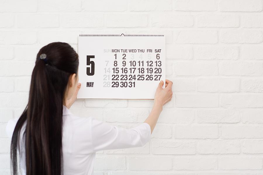 Woman hanging calendar on wall Photograph by Image Source