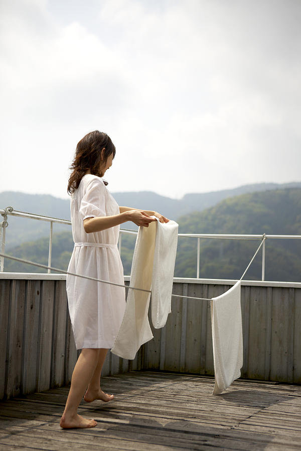 Woman hanging laundry on clothes line on wooden patio Photograph by Ultra F