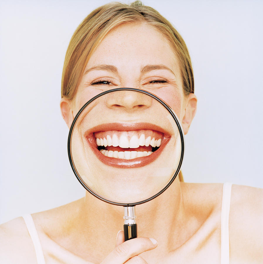 Woman holding magnifying glass in front of mouth, smiling, portrait Photograph by Pando Hall